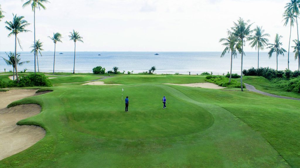Golfer preparing to putt on the lush green course of Laguna Golf Bintan, surrounded by tropical beauty.