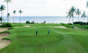 Golfer preparing to putt on the lush green course of Laguna Golf Bintan, surrounded by tropical beauty.